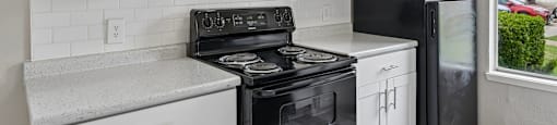 A black refrigerator stands next to a stove in a kitchen with white cabinets.