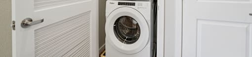 A white washing machine is stacked on top of another in a small laundry room.