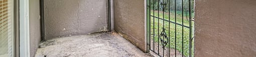 A patio with a metal gate and a view of a green forest.