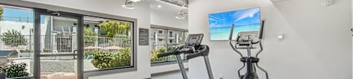 A gym with treadmills, elliptical machines, and a flat screen TV.