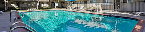 A swimming pool in front of a building with trees and sun loungers.
