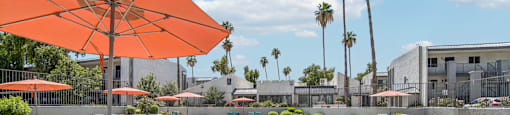 A pool area with a large orange umbrella and lounge chairs.