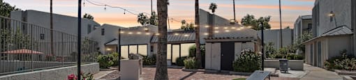 A sunset view of a courtyard with palm trees and a building in the background.