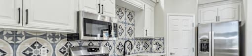 A kitchen with white cabinets and a black and white tiled backsplash.