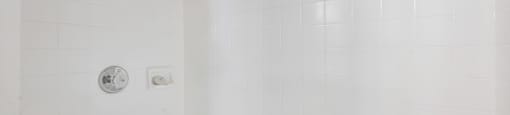 A white tiled shower with a shower head and a faucet.