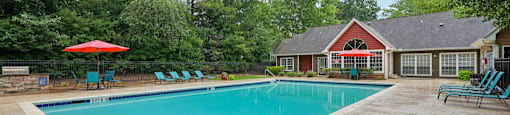 A pool with a red umbrella and a house in the background.