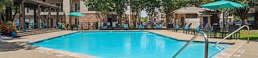 A large swimming pool surrounded by trees and a building in the background.