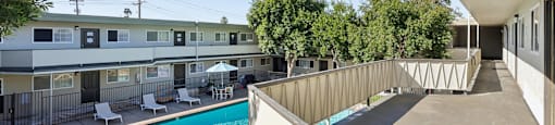 A swimming pool is surrounded by a concrete patio and a white building.