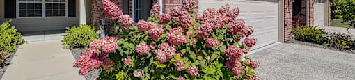 the front of a house with a garage door and pink flowers