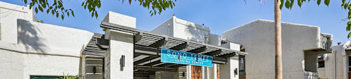A building with a blue awning is surrounded by plants and trees.