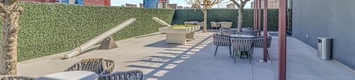 A patio with tables and chairs is surrounded by a wall and trees.