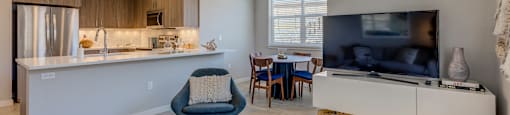 a living room and kitchen with a large tv on the wall and a dining area in the