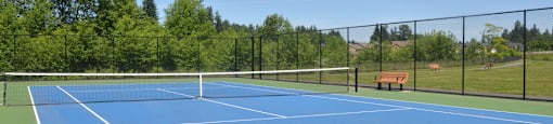 A blue tennis court surrounded by a black fence.