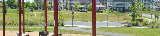 A playground with a red swing set in the foreground and apartment buildings in the background.