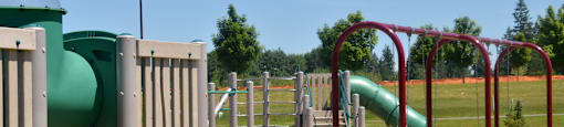A playground with a green slide and a red swing set.