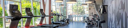 a gym with cardio equipment and windows in the lobby of a building