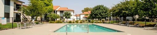 Apartments for Rent Mesa AZ - Mesa Station - Hot Tub and Pool Area with Lounge Chairs, Tables with Chairs, and Lush Greenery Surrounding