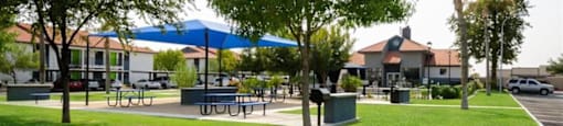 a park with tables and umbrellas and houses in the background