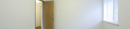 A room with a carpeted floor, a door, and a window with blinds.