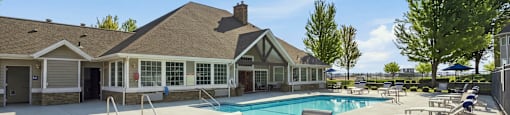 A pool area with a table and chairs in front of a house.