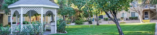 A gazebo is surrounded by greenery and a well-kept lawn.