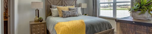 One Bedroom Apartments in Georgetown Texas - Williamson at the Overlook - Furnished Bedroom with Bed, Wood-Style Frame, Nightstand, and Dresser, with Window, Ceiling Fan, Carpetted Floors, and Attached Bathroom View