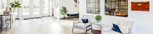 A well-lit, spacious lobby with a white sofa, wooden chairs, and a glass table.