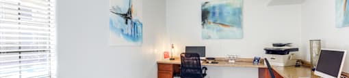 A room with a desk, chairs, and artwork on the wall.