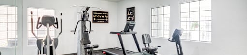 A gym with a green treadmill, a white wall, and a ceiling fan.