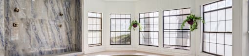 Senior Housing In Paradise, Las Vegas, NV - Gramercy Parc - Indoor Pool Area With A Round Pool, Large Windows, Metal Handrail, Hanging Plant, and A Marble Wall with Built-In Showers.