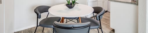 Dog-Friendly Senior Apartments In Paradise, Las Vegas, NV - Gramercy Parc - Kitchen With Wood-Style Plank Flooring, Cabinets, Countertops, Modern Appliances, Table With Chairs, And A Ceiling Fan.