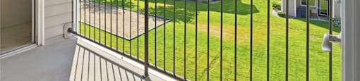 A balcony with a black railing overlooks a grassy area and apartment buildings.