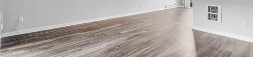 Three-Bedroom Apartments in San Jose, CA - Los Gatos Creek - Empty Living Room with Wood-Style Flooring, Light Gray Walls, White Baseboards, Vent, Electrical Outlets, Light Fixture, and a Glass Door.