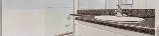One Bedroom Apartments in San Jose CA - Los Gatos Creek - Bathroom with Small Window, Dark Countertops, and White Cabinetry