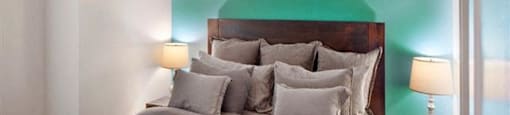 Portland, OR, Dog-Friendly Apartments - The Beverly - Bedroom with Carpeted Floor, Bed, Nightstands with Lamps, Dresser, and Green Accent Wall.