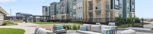 Georgetown Texas Apartments - Williamson at the Overlook - Outdoor Seating Lounge with Building Exterior, Surrounding Greenery and Path in the Background