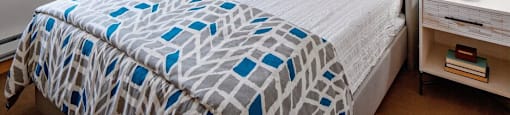 A bed with a blue and white patterned comforter and two green pillows.
