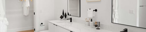A white bathroom with a toilet, sink, and mirror at The Laura apartment complex in Houston, TX.