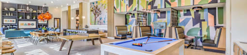 a game room with a pool table and tables in front of a colorful wall