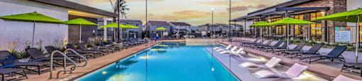 a resort style swimming pool with lounge chairs and umbrellas