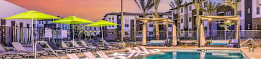 a swimming pool with chaise lounge chairs and umbrellas in front of an apartment building