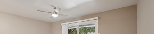 an empty living room with a large window and a ceiling fan