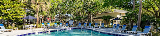 a swimming pool with chaise lounge chairs and trees in the background