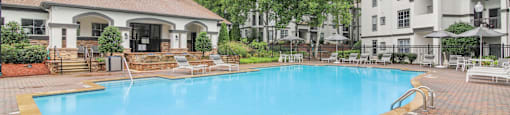 A large outdoor swimming pool surrounded by a brick patio and lounge chairs.