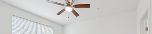 A room with a ceiling fan and a window with blinds.