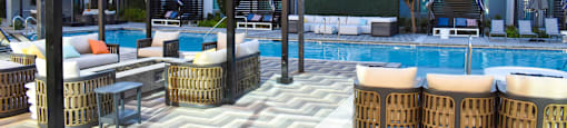 A pool area with a white and grey tiled floor and a white pool surrounded by chairs and tables.