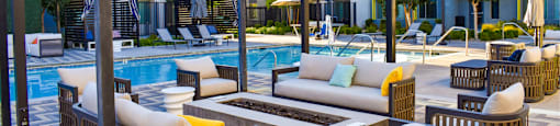 A poolside seating area with a large pool and apartment buildings in the background.