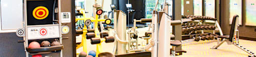 A gym with a variety of equipment including dumbbells, weight plates, and a bench press.