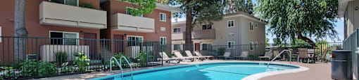 Three-Bedroom Apartments in Milpitas, CA - Spring Valley - Gated Swimming Pool with Lounge Seats, Table, Chairs, Surrounded by Trees and Apartment Buildings.