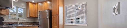 Two-Bedroom Apartments in Milpitas, CA - Spring Valley - Modern Kitchen with Stainless Steel Appliances, Wood-Style Cabinetry, Hanging Lights, Grey Tile Flooring, Granite Countertops, and Large Windows.